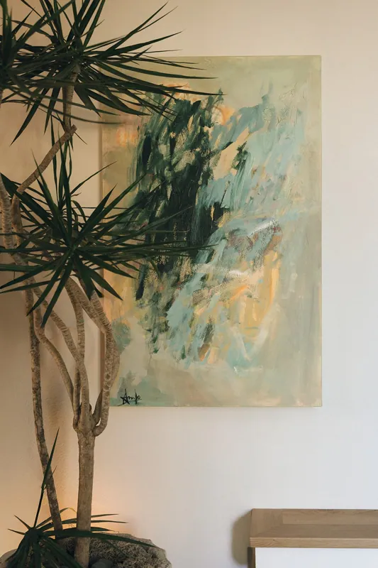 Sunlit corner with a large indoor tree beside a soft abstract painting in greens.