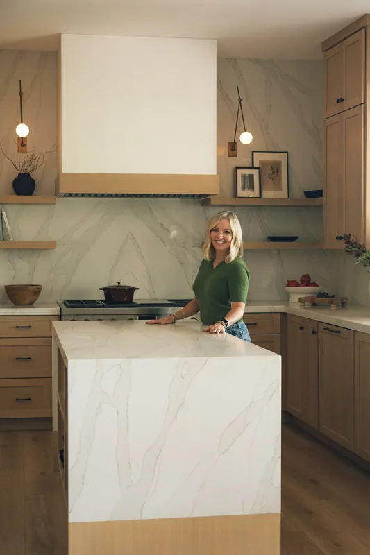 Meredith Gough seated on a white marble waterfall island in a bright, airy kitchen.
