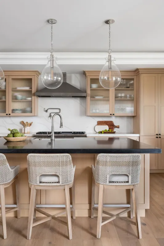 Bright modern kitchen with light wood cabinetry, black countertop island, and two hanging glass pendant lights.