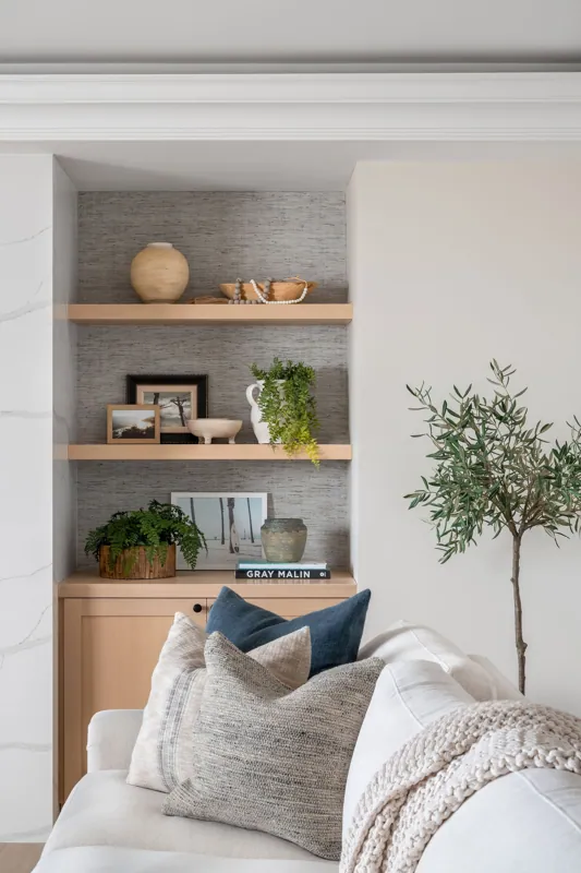 Living room shelf with decorative items, framed photos, plants, and a couch with pillows and a knitted throw blanket.