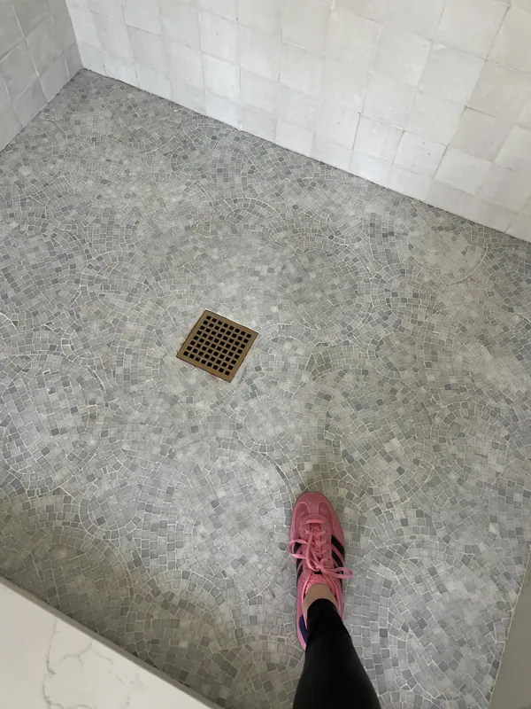 Detail of a marble shower threshold meeting small-format mosaic floor tile.