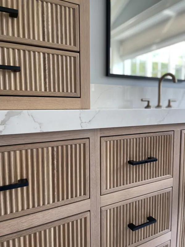 Reeded wood vanity cabinetry with matte-black hardware below a framed mirror.