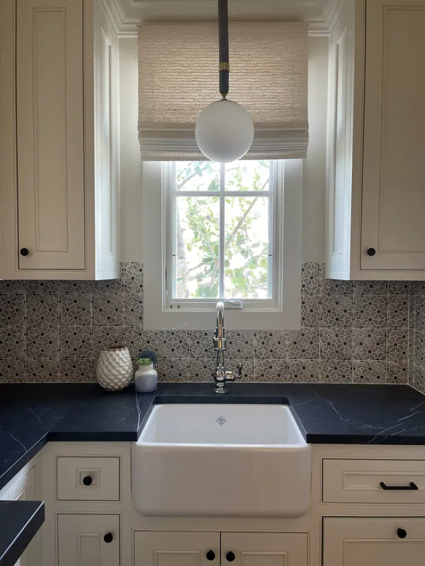 Laundry room with a farmhouse sink, deep navy countertop, white cabinetry, and a sunny window.
