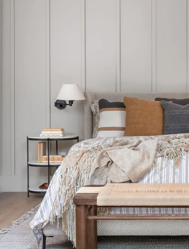 Serene bedroom with layered neutral bedding, a dark upholstered headboard, wood nightstands, and wall-mounted reading sconces.
