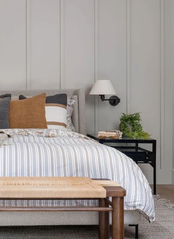 Bedroom with crisp striped bedding, a wood bench at the foot of the bed, and a nightstand styled with branches.